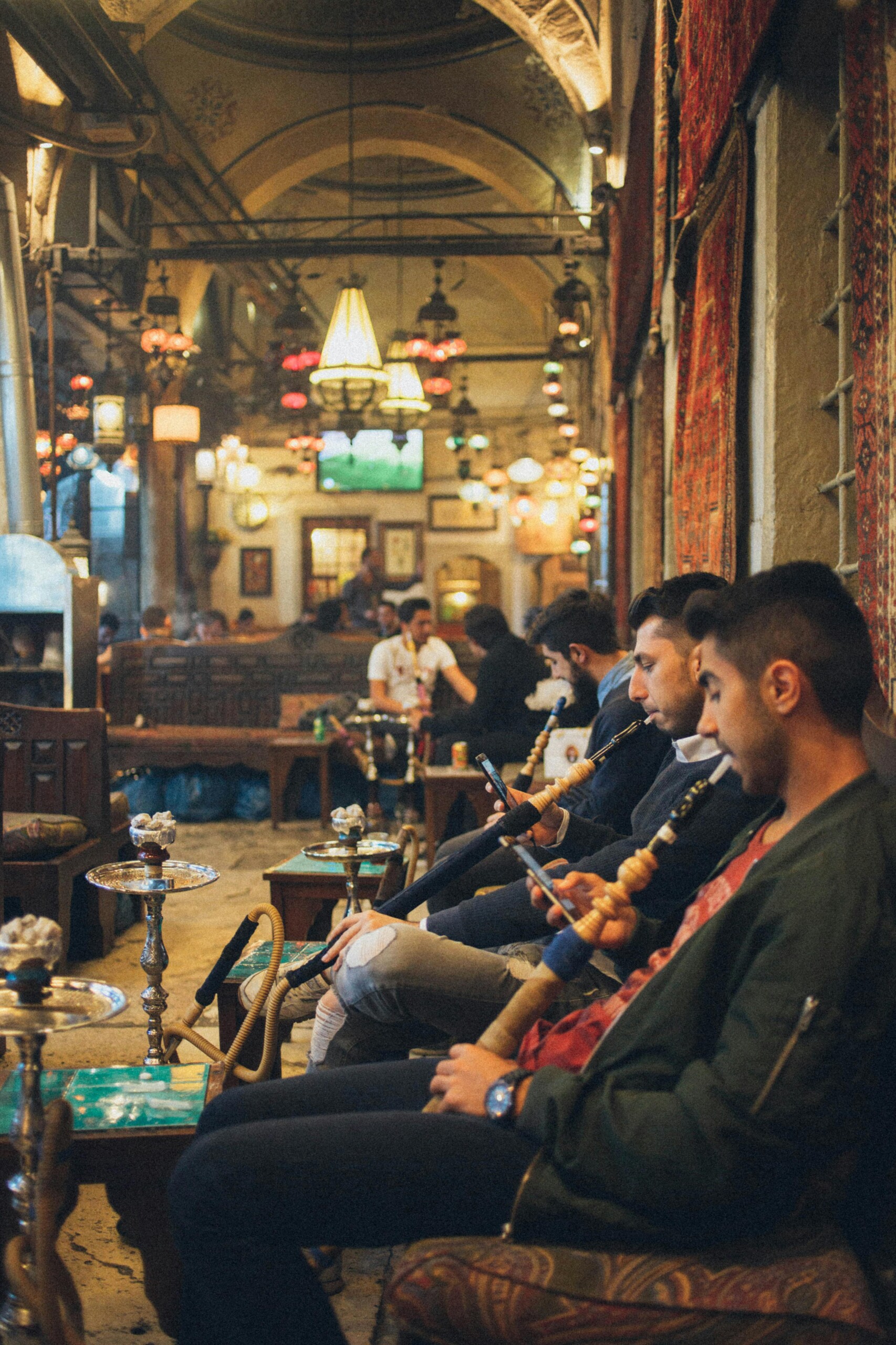 Group of young men relaxing with hookahs in a cozy, vibrant indoor lounge setting.